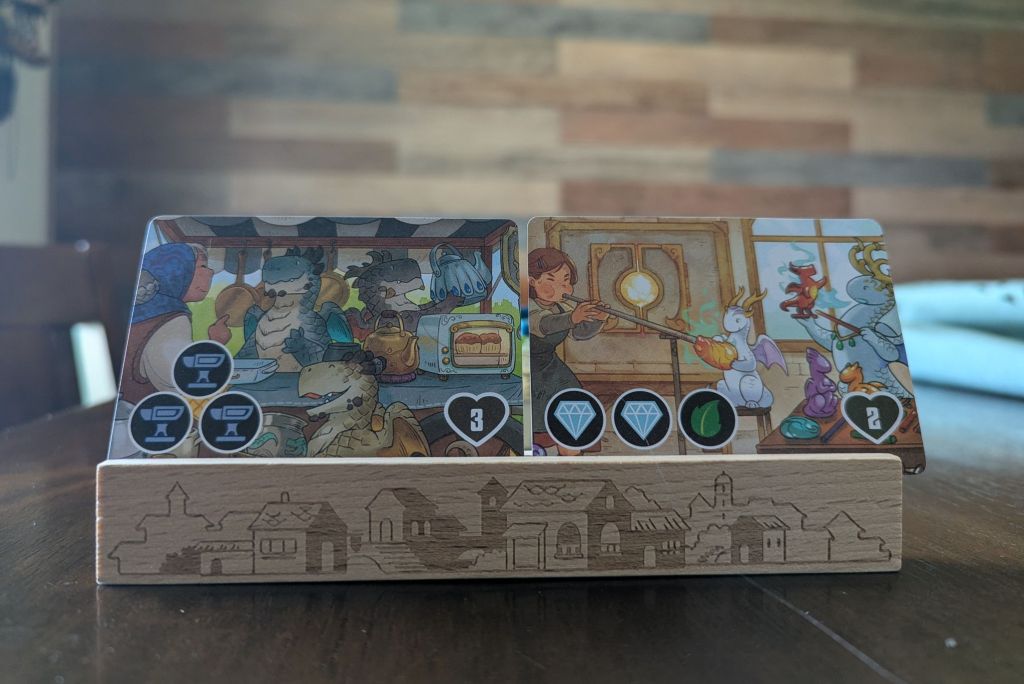 a player's hand set atop the included card holders. one shop requires three metal dragons in a triangle while the other requires two crystal dragons followed by a leaf dragon.